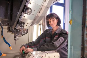 Eine Mitarbeiterin steht an einer Maschine und lächelt | © Wendelstein Werkstätten