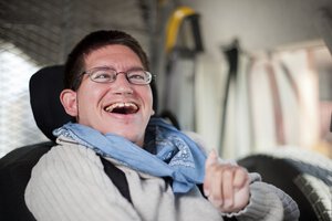 Ein junger Mann mit Behinderung sitzt in einem Fahrzeug und lacht | © Caritas München und Oberbayern