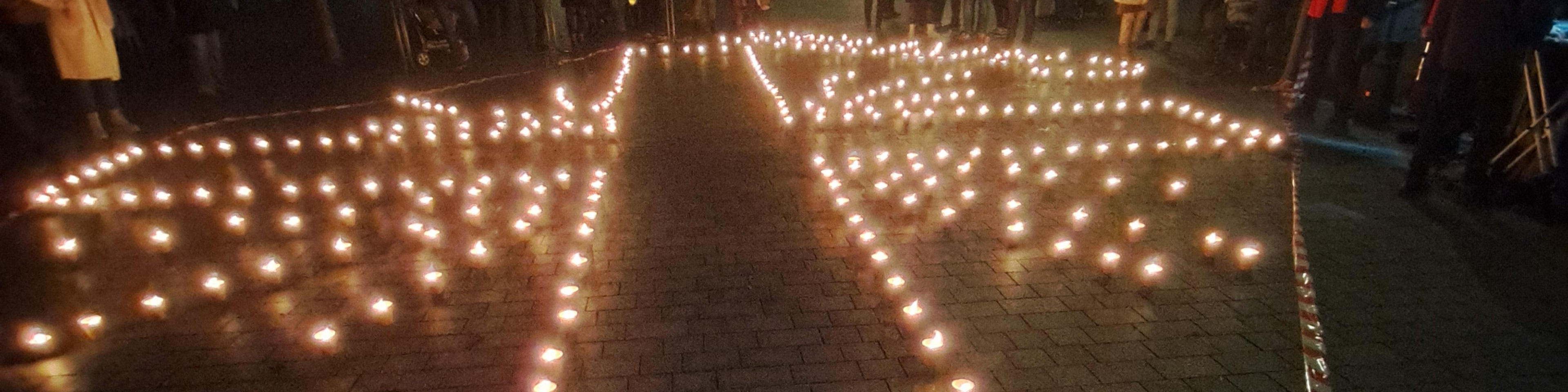 Kerzen auf einem Platz in München formen das Caritas-Flammenkreuz | © Caritas München-Freising