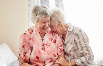 Aufnahme von zwei glücklichen älteren Frauen, die sich zu Hause umarmen | © PeopleImages - iStock