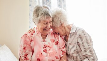 Aufnahme von zwei glücklichen älteren Frauen, die sich zu Hause umarmen | © PeopleImages - iStock